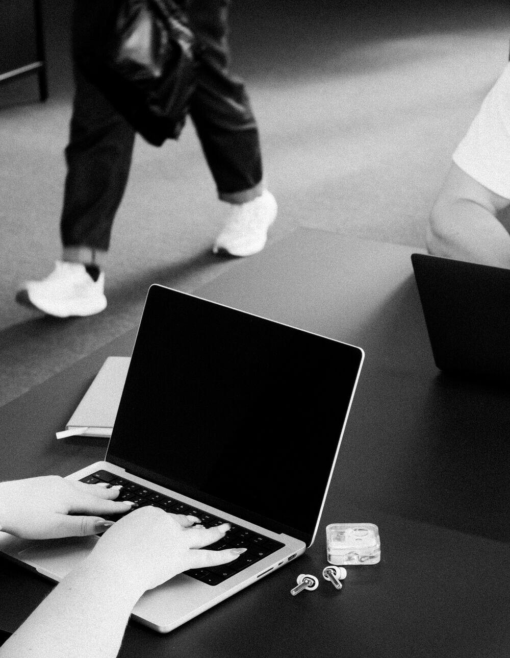 Hands typing on a laptop while a colleague passes behind