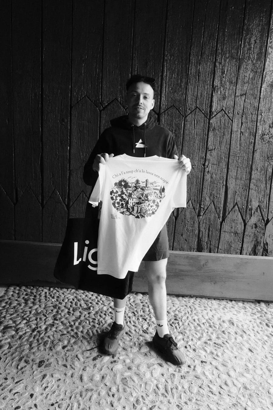 A teammate posing with a Light tote bag and t-shirt against a wooden wall