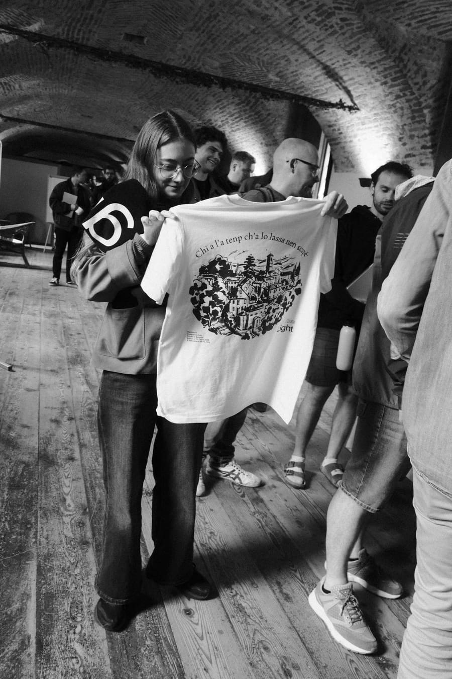 A teammate showing off a Light t-shirt to a small crowd indoors