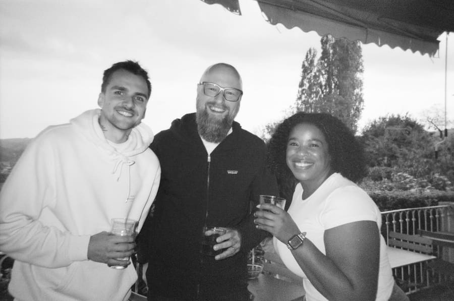 Three teammates smiling with drinks on a rooftop terrace at dusk